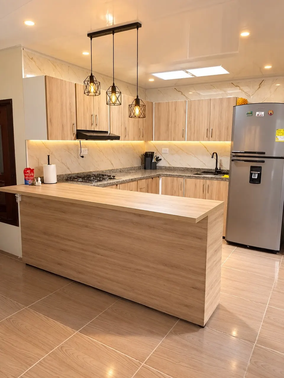 Cocina integral en tono madera con barra al frente, muebles altos y bajos y lámparas colgantes
